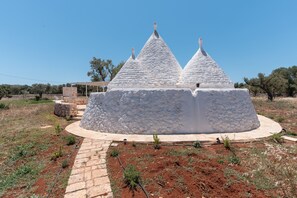 Une structure conique blanche, à base circulaire, entourée d’un sentier pavé et d’une végétation clairsemée.