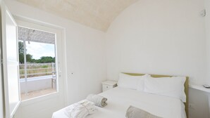 A bedroom with a bed, a nightstand, a window with a view, and a door. - Villa 'Trullo White Dream Con Piscina' with Private Pool, Wi-Fi and Air Conditioning (Ostuni)