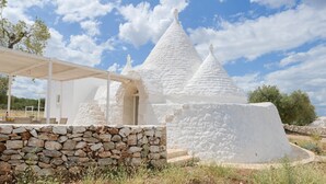 A white stone structure with conical roofs, a stone wall, and a covered seating area. - Villa 'Trullo White Dream Con Piscina' with Private Pool, Wi-Fi and Air Conditioning (Ostuni)