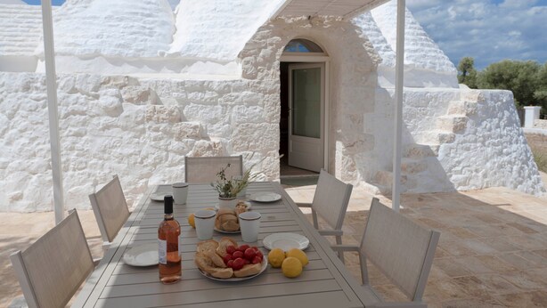 A table set outdoors with a white tablecloth, plates, a bottle, and a bowl of fruit. - Villa 'Trullo White Dream Con Piscina' with Private Pool, Wi-Fi and Air Conditioning (Ostuni)