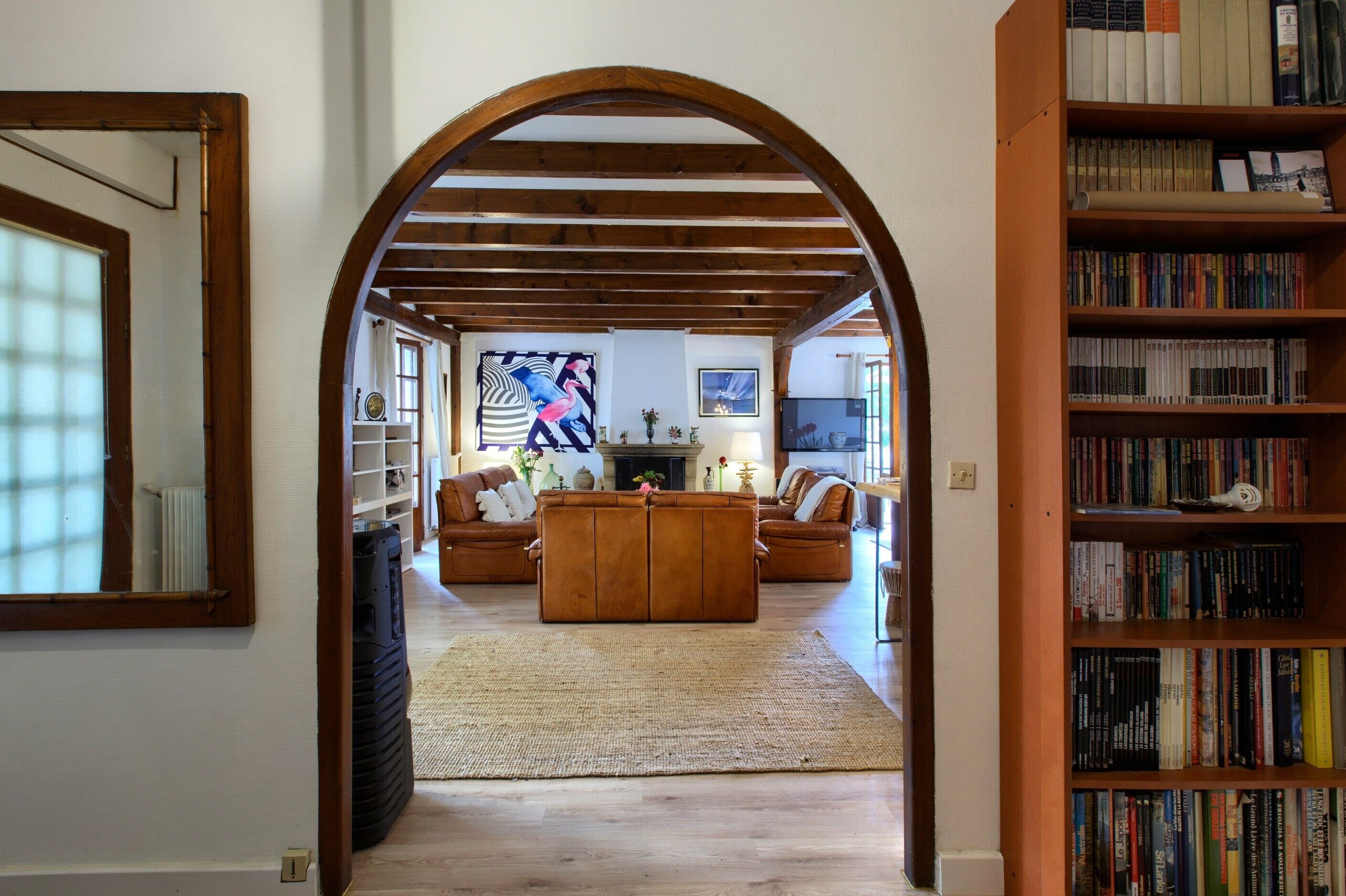 An interior with a wooden archway, a sofa, a rug, and a bookshelf.