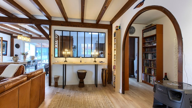 A cozy living room with a wooden ceiling, a large window, a bookshelf, and a Sony entertainment system. - Villa 'Rodolphe' with Private Pool, Private Terrace, and Wi-Fi (Le Pian-Médoc)