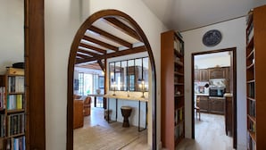 A hallway with wooden bookshelves, a kitchen area, and a dining area with a table and chairs. - Villa 'Rodolphe' with Private Pool, Private Terrace, and Wi-Fi (Le Pian-Médoc)
