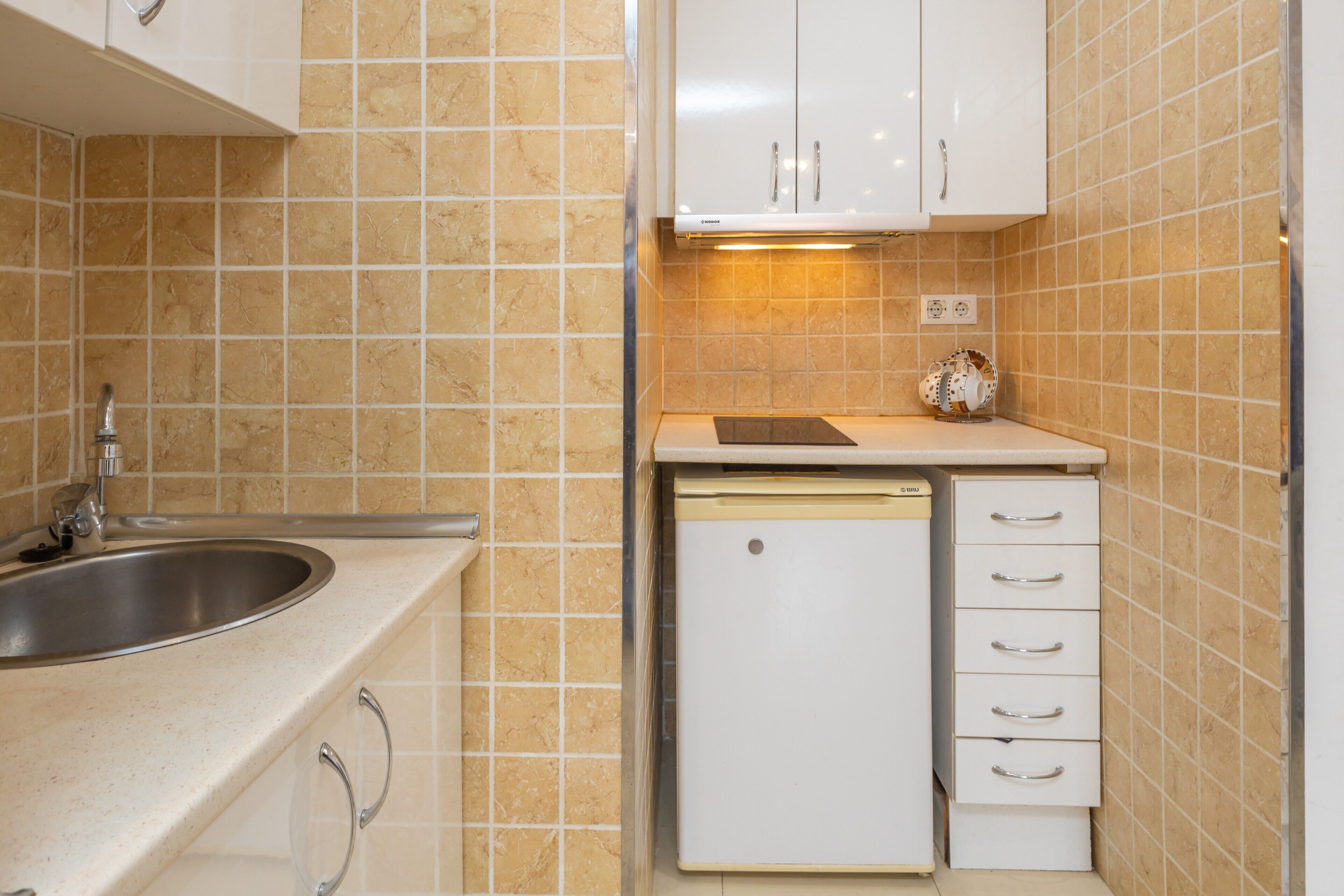 A compact kitchen with a sink, dishwasher, and white cabinets.