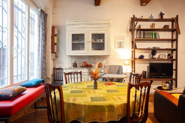 A cozy living room with a red sofa, a dining table with a yellow tablecloth, a bookshelf, and a television.