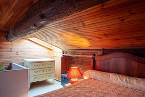 A wooden ceiling, a bed with a headboard, a nightstand, a dresser, and a lamp.