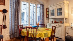 A dining area with a table set for four, a window with metal bars, and a white cabinet with glass doors. - Holiday Home 'Maison À Sigean' with Wi-Fi (Sigean)