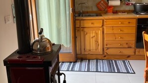 A compact kitchen with wooden cabinets, a stove, and a window with curtains.