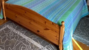 A wooden bed with a striped bedspread, a nightstand with a lamp, a dresser with framed photos, and a patterned rug.