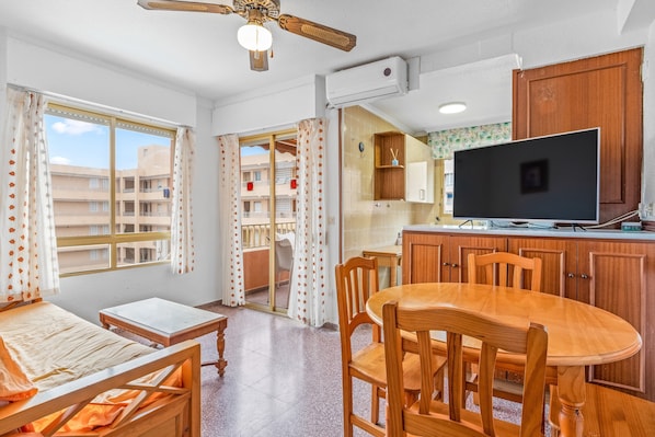 A room with a bed, a table, chairs, a TV, and a ceiling fan.