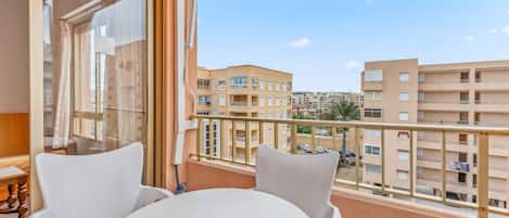 A balcony with a table and chairs, a view of neighboring buildings, and a clear sky.