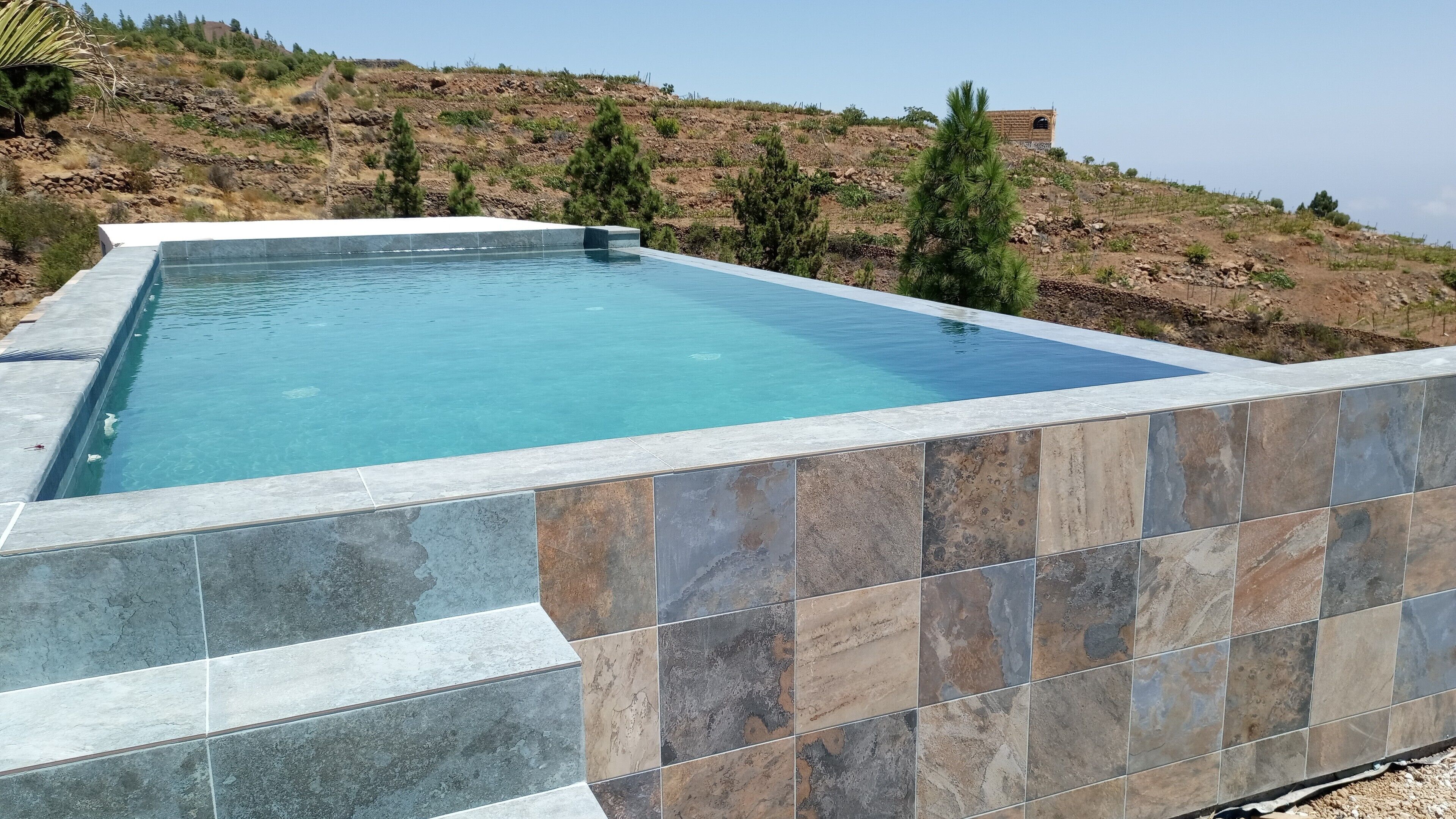Una piscina rectangular con borde de azulejos, rodeada por un paisaje montañoso.