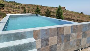 Una piscina rectangular con borde de azulejos, rodeada por un paisaje montañoso.