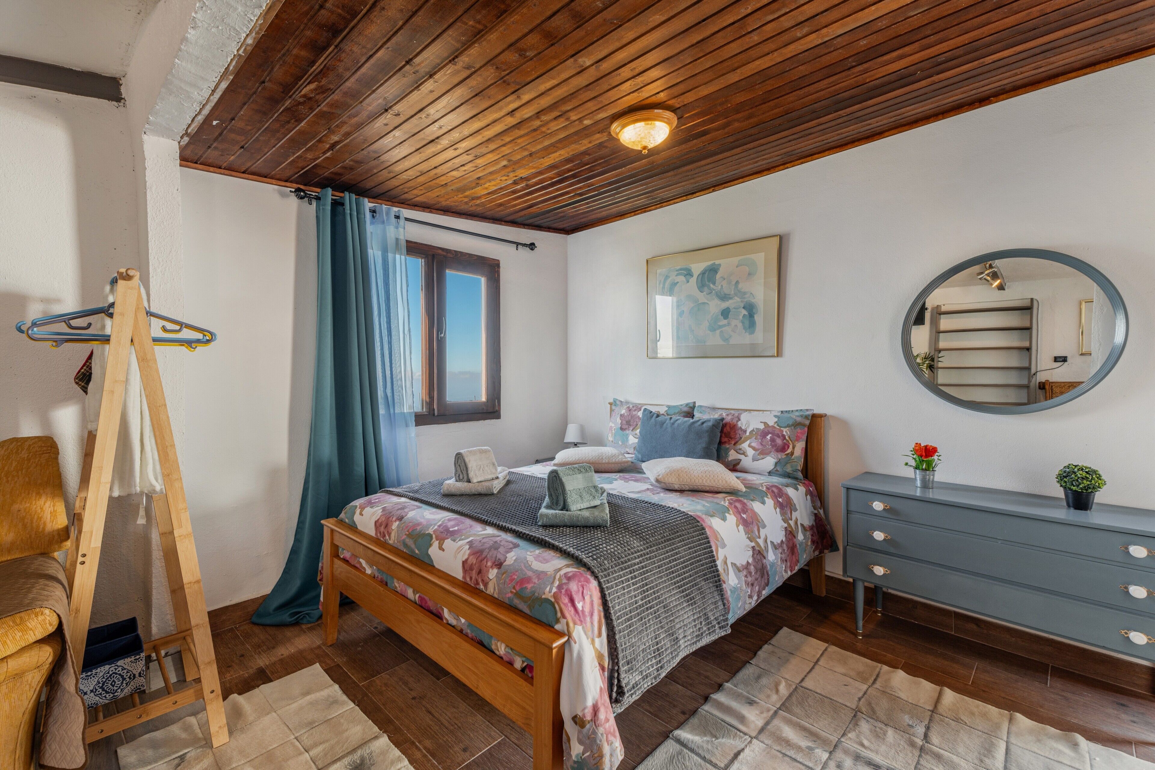 A bedroom with a wooden bed, a dresser, a mirror, and a painting on the wall.
