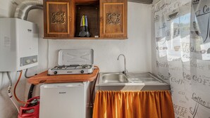 Cocina compacta con estufa a gas, pileta, refrigerador y un armario con utensilios de cocina.