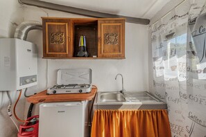 Cocina compacta con estufa a gas, pileta, refrigerador y un armario con utensilios de cocina.