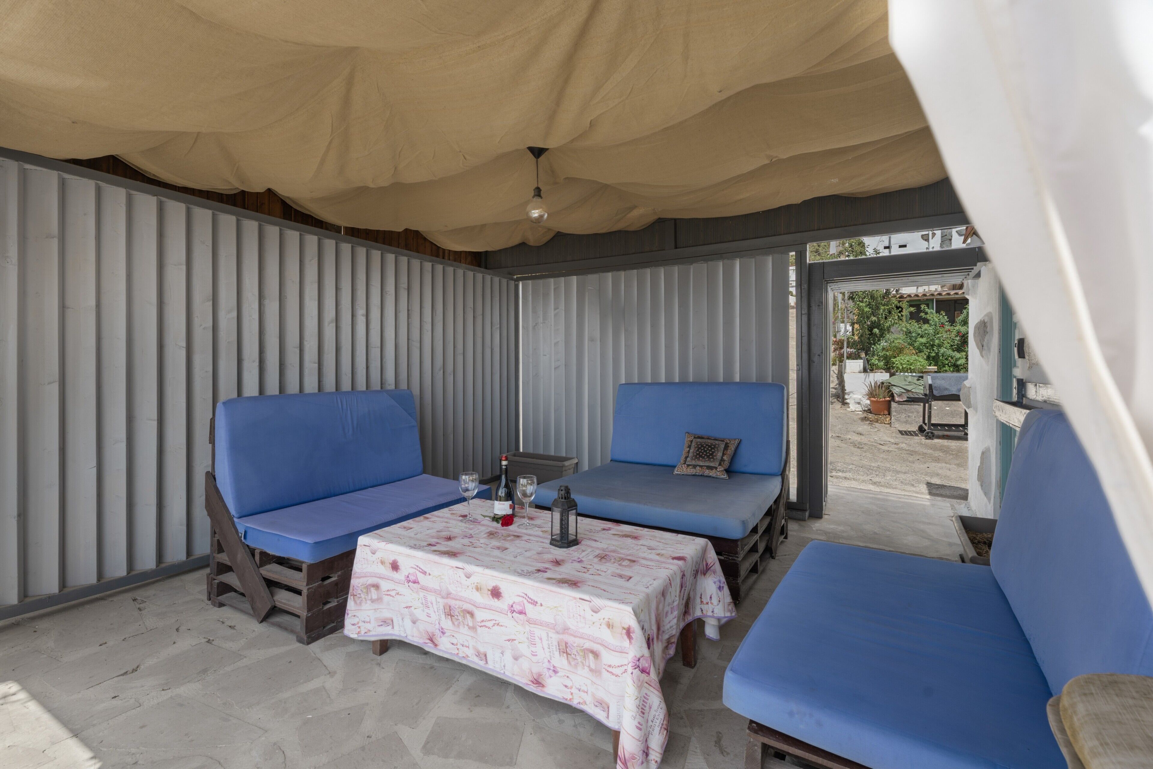 An outdoor patio with blue cushioned seating, a table with a floral tablecloth, and a ceiling fan.