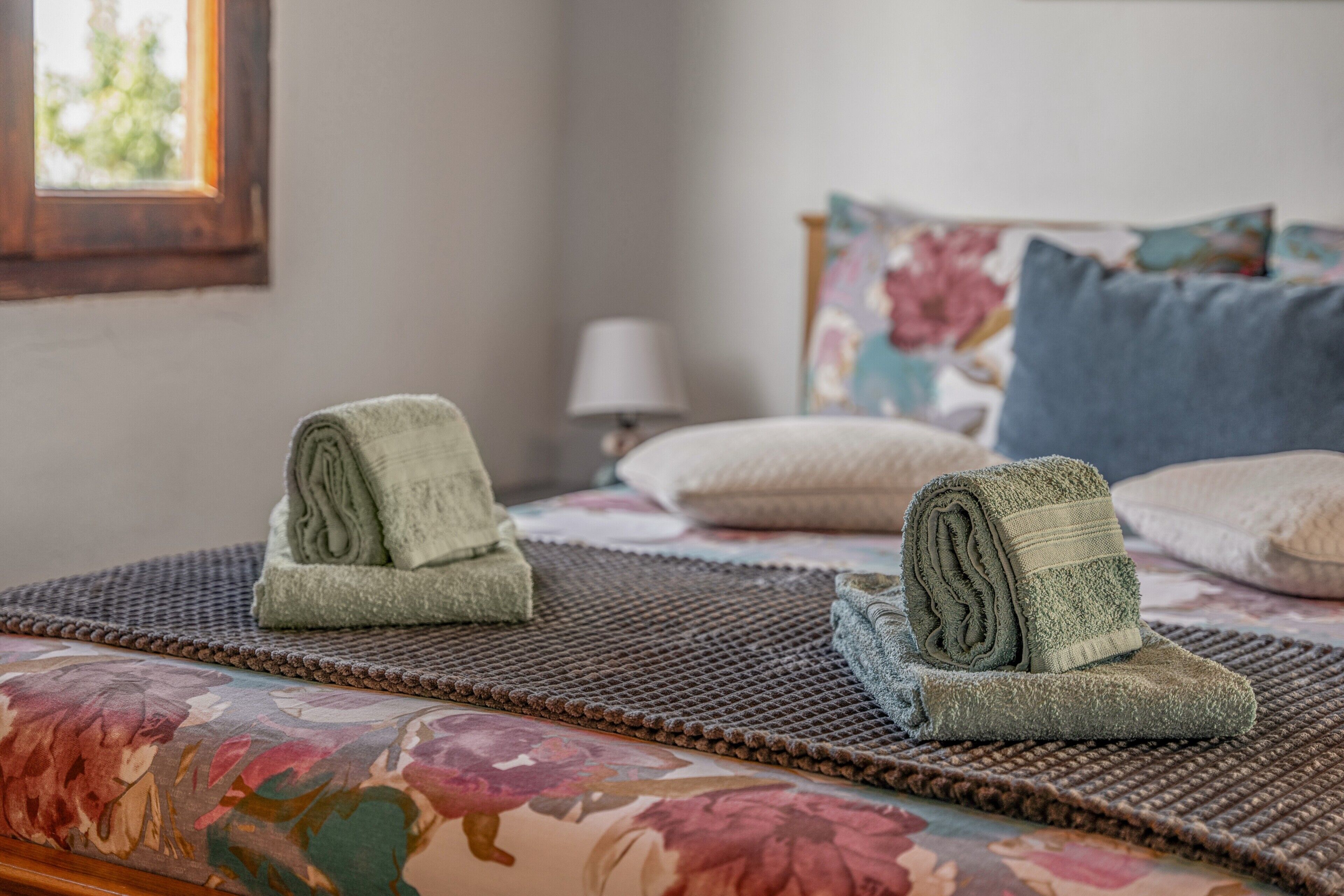 A bed with floral bedding, a textured rug, and rolled towels.
