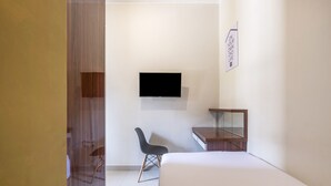 Quarto de hotel moderno com cama, escrivaninha, cadeira e televisão de tela plana na parede.