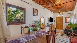 A dining area with a wooden table, chairs, a vase of flowers, a wooden ceiling, and a television in the background. - Vacation Home 'Land Of Dreams' with Sea View, Shared Pool and Wi-Fi (Cruz de tea)