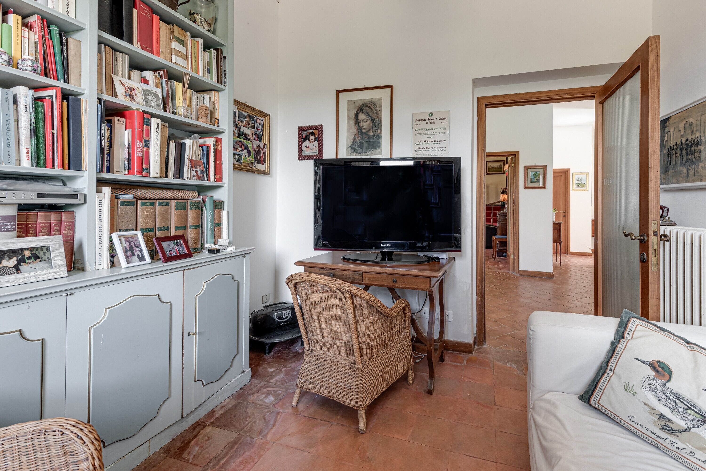 A living room with a bookshelf, a television, a wicker chair, and a white sofa.