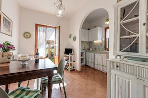 Il y a un coin repas avec une table, des chaises et un téléviseur. La cuisine est équipée de placards et d’une fenêtre.
