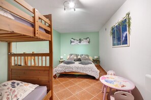 Ein Zimmer mit einem Etagenbett, einem Einzelbett, einem kleinen Tisch mit einer Disney-Unterlage und einem an der Wand hängenden Bild.