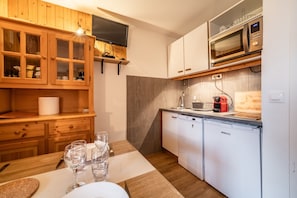 A compact kitchen with wooden cabinets, a microwave, a dishwasher, and a flat-screen TV mounted above the counter. - Apartment 'Morillon' with Mountain View and Balcony (Morillon)