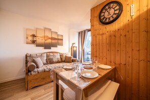 A cozy room with a wooden wall, a wooden sofa, a dining table set with plates and glasses, and a wall clock. - Apartment 'Morillon' with Mountain View and Balcony (Morillon)
