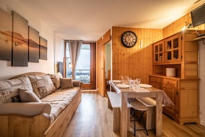 A cozy living room with a wooden sofa, a dining table set with plates and glasses, and a wooden cabinet with glass doors. - Apartment 'Morillon' with Mountain View and Balcony (Morillon)