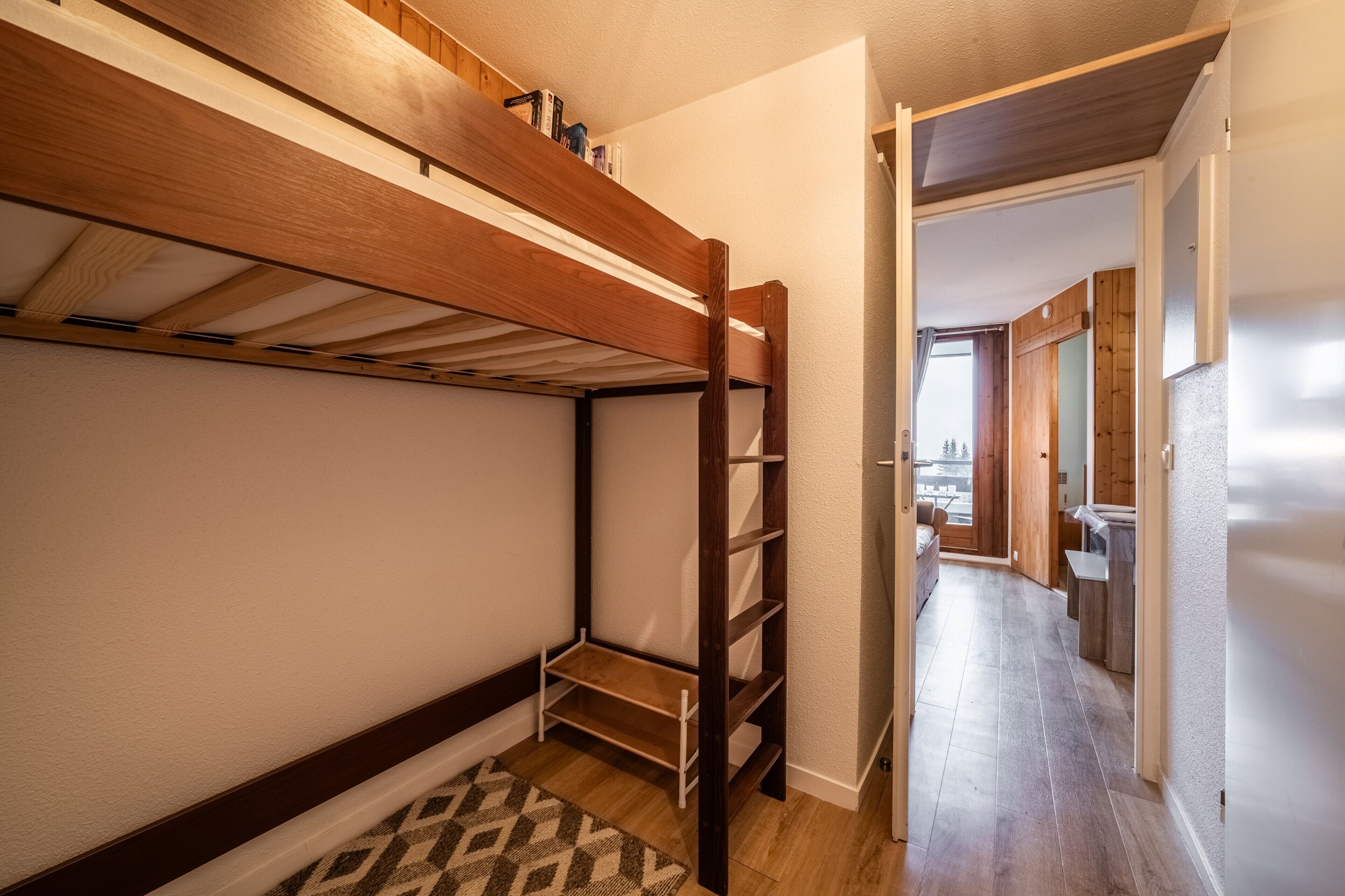 A bunk bed with a ladder, a patterned rug, and a hallway leading to a dining area.