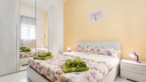 Een slaapkamer met een bed, nachtkastje, spiegel en een aan de muur hangend schilderij.
