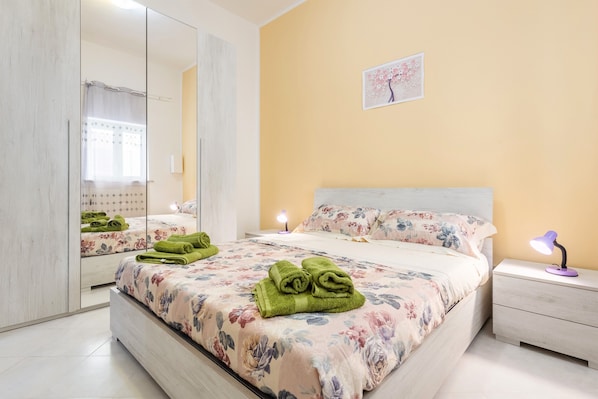 A bedroom with a bed, a nightstand, a mirror, and a wall-mounted picture.