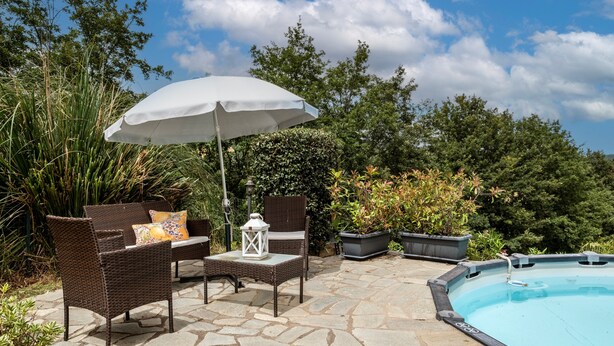 A patio with wicker furniture, a white umbrella, and a swimming pool.