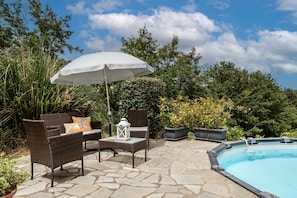 Un patio con mobiliario de mimbre, una sombrilla blanca y una piscina.