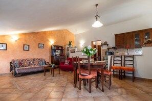 Una sala de estar con sofá, mesa de comedor, sillas, zona de cocina y un sofá rojo.