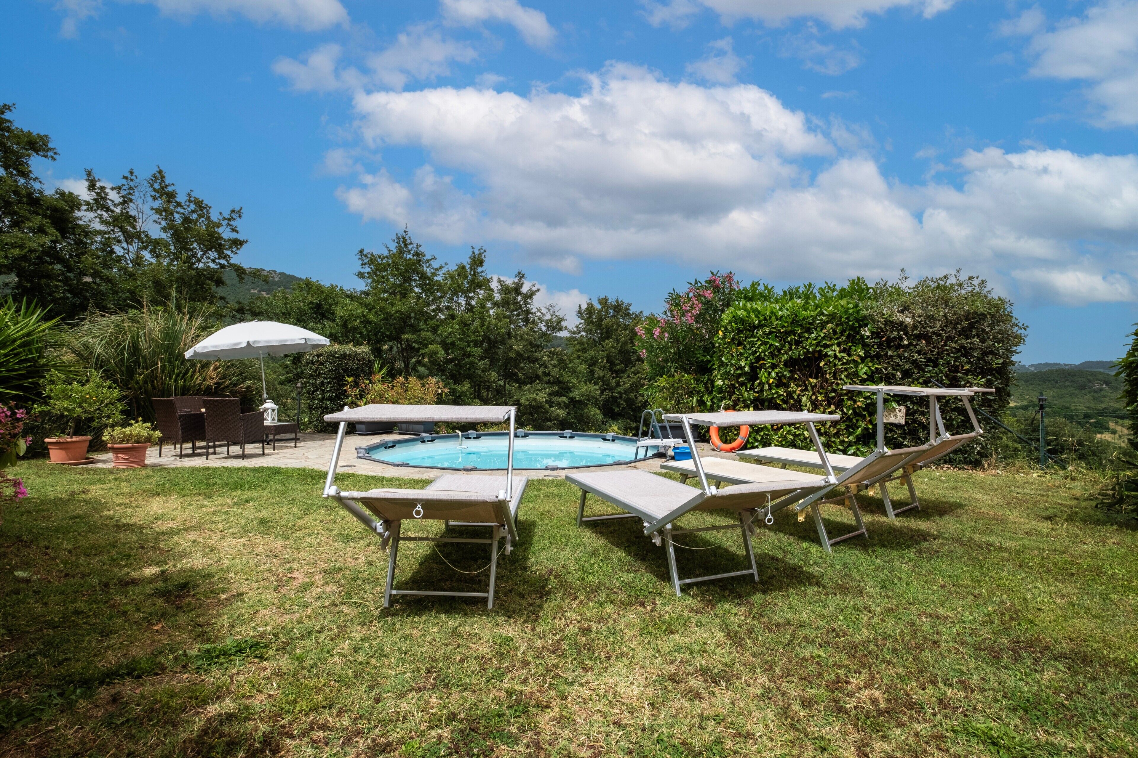 Un giardino sul retro con piscina, sedie a sdraio e un tavolo sotto un ombrellone.