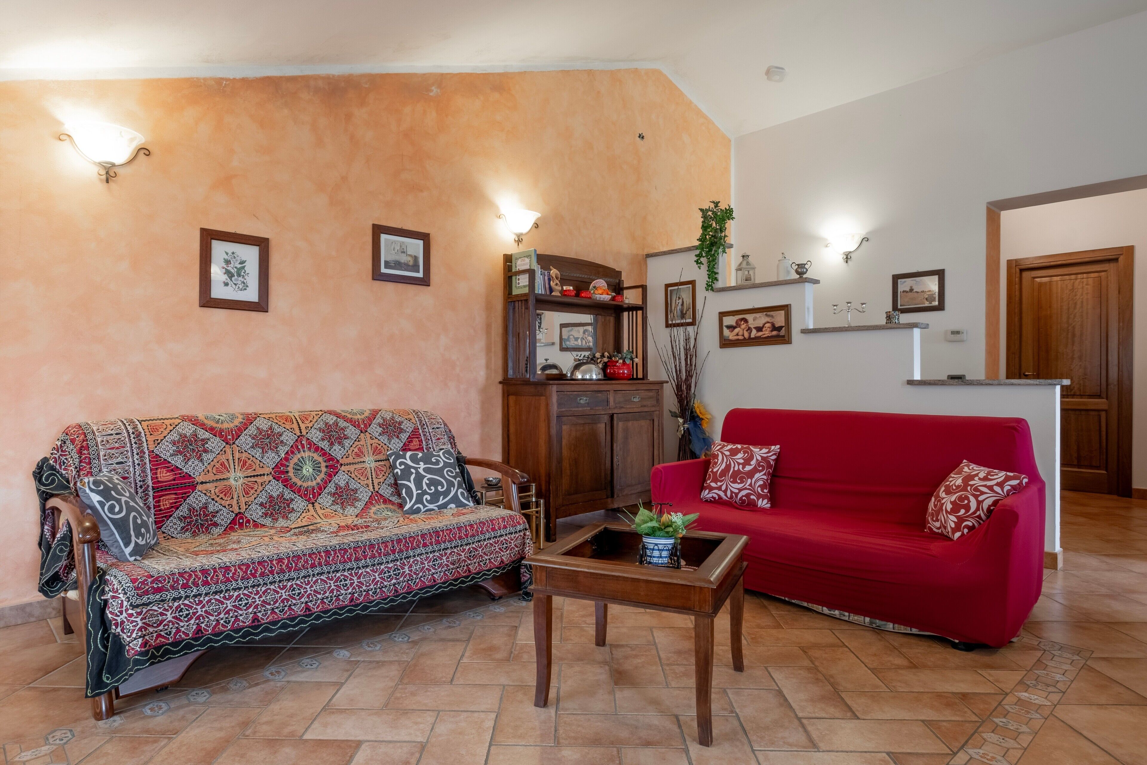 Un salon avec un canapé à motifs, un canapé rouge, un meuble en bois et des étagères murales ornées d’objets décoratifs.