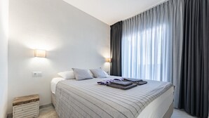 A neatly made bed with a striped blanket, two bedside lamps, and a window with dark curtains. - Holiday Apartment "Casa Feliz" with Shared Pool, Private Terrace & Wi-Fi (Mijas)