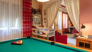 Ein Billardtisch mit Kugeln, ein roter Sessel, eine Lampe und ein Tisch ebenfalls mit einer Lampe.