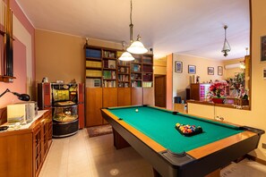 A pool table with balls, a bookshelf, and a billiard cue rack.