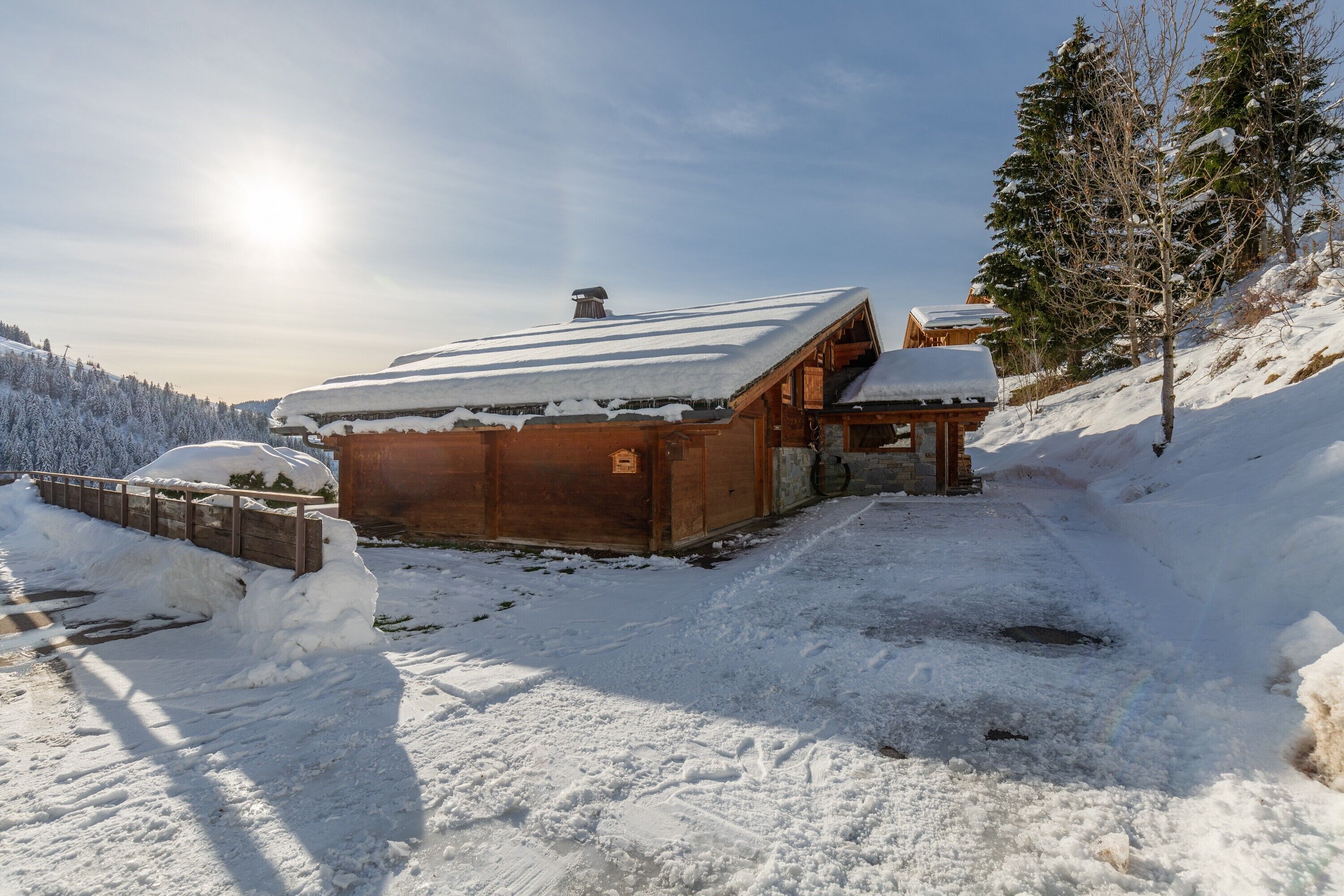 Una cabaña de madera con techo cubierto de nieve, rodeada de árboles nevados y un cielo despejado.
