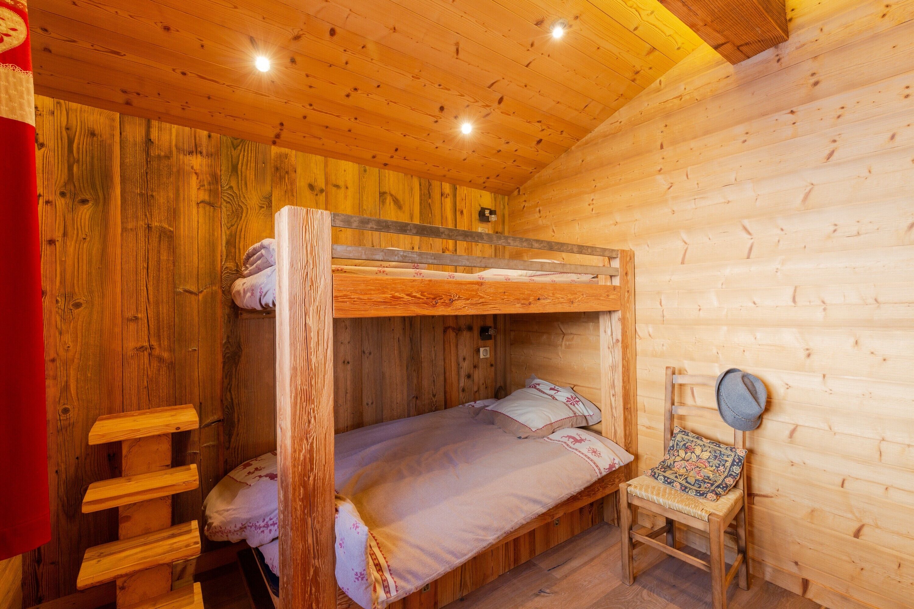 Ein Stockbett mit einer Leiter, ein Holzstuhl mit Hut und ein kleiner Tisch mit Lampe.