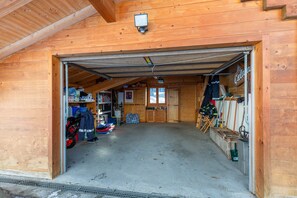 Un bâtiment en bois avec une porte de garage ouverte, dévoilant un espace de rangement contenant divers objets et un vélo.