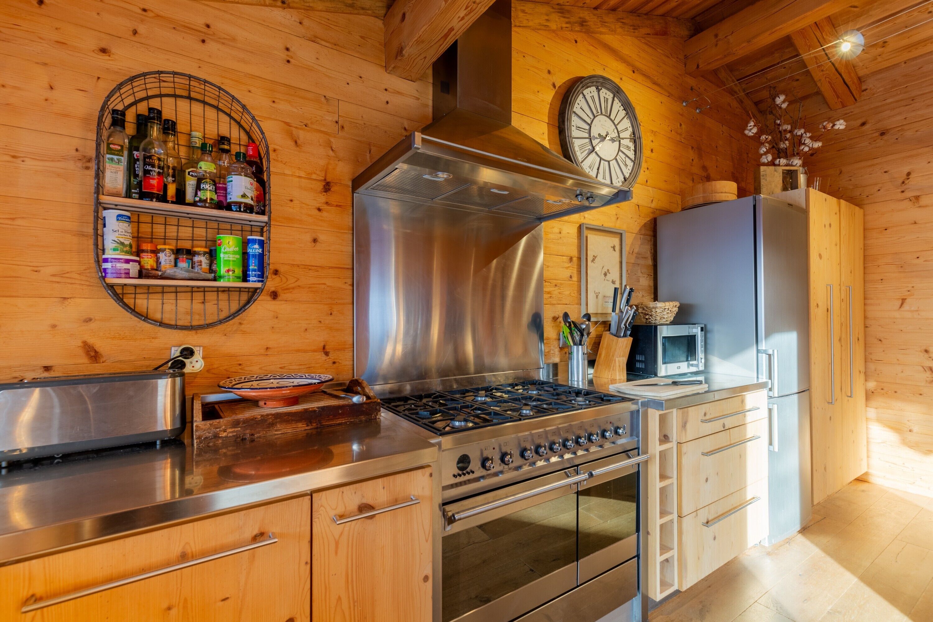 A kitchen with wooden walls, stainless steel appliances, a clock, and a microwave.