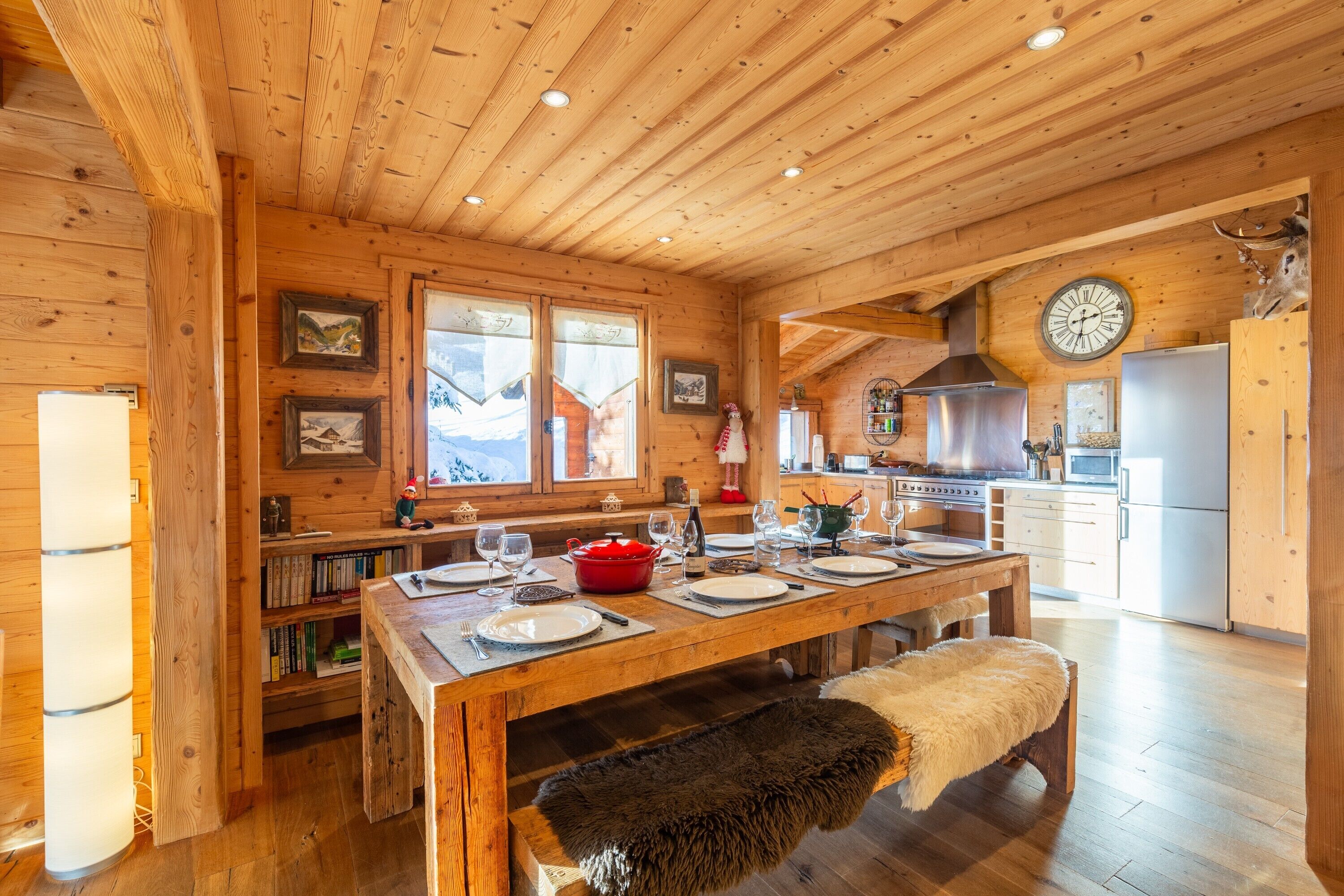A wooden cabin interior with a dining table set for four, kitchen appliances, and framed pictures on the walls.
