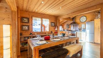 A wooden cabin interior with a dining table set for four, kitchen appliances, and framed pictures on the walls.