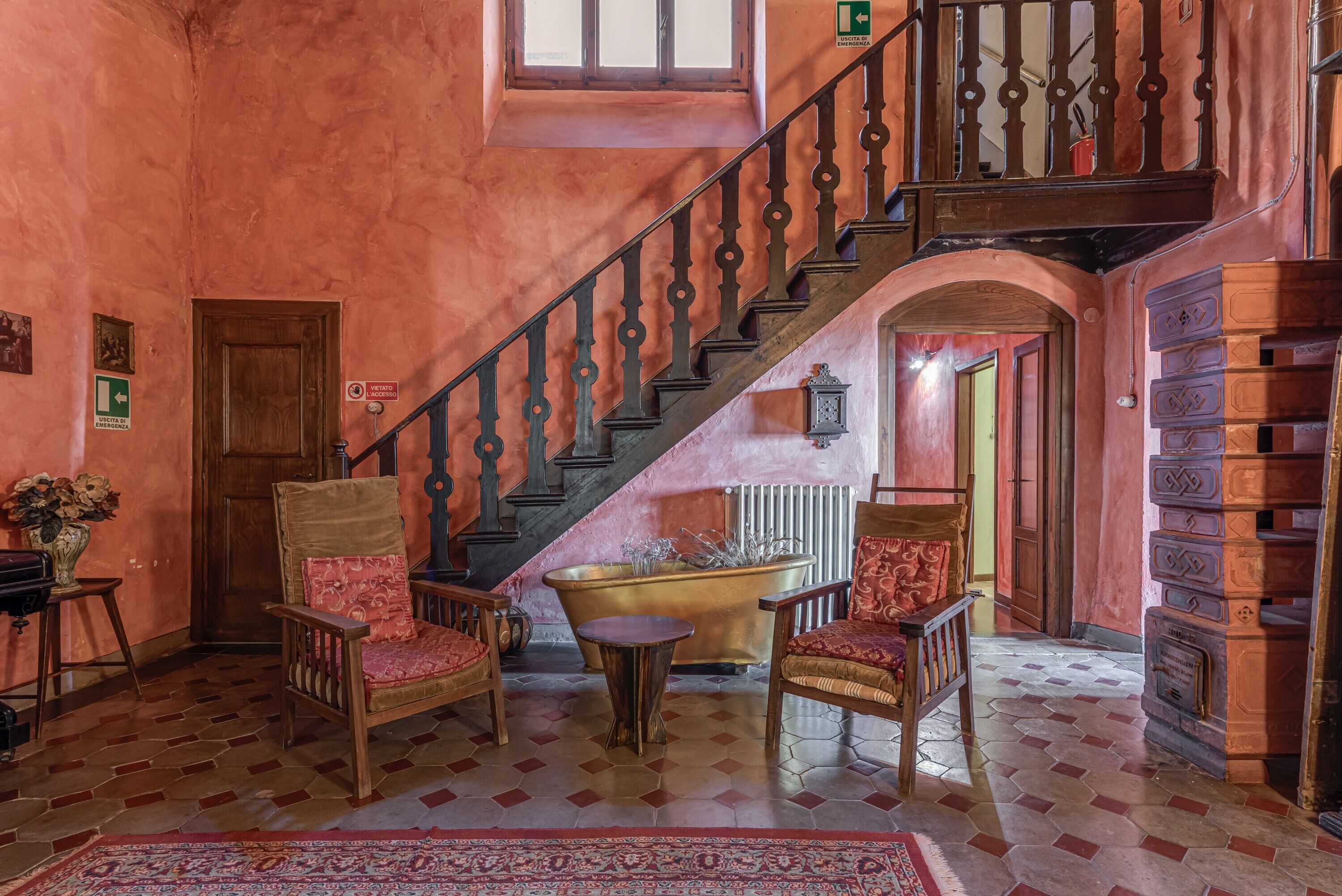 A staircase with a wooden railing, a bathtub, and two wooden chairs with cushions.