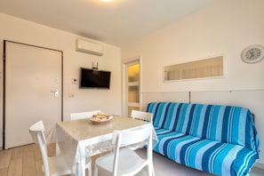 Um quarto pequeno com uma mesa, cadeiras, um sofá, uma televisão e um relógio na parede.
