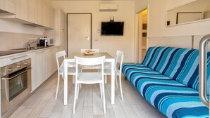 A compact kitchen with a dining table, chairs, a sofa, and a TV. - Holiday Home 'Villafranca' with Sea View, Wi-Fi and Air Conditioning (Alghero)